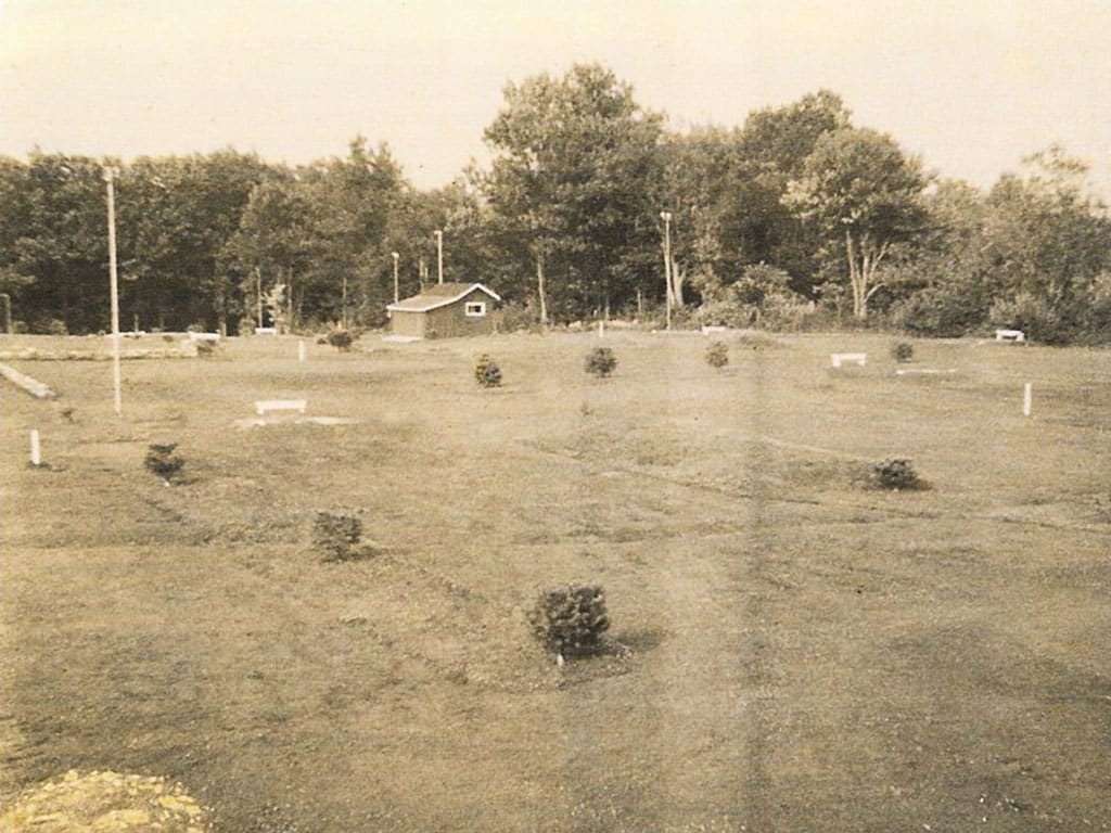 Early photo of golf course with small trees and shed in background