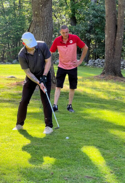 Player does a practice swing for a chip shot while teammate watches from behind