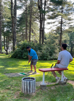 Player stands ready to tee off while teammate waits his turn on bench