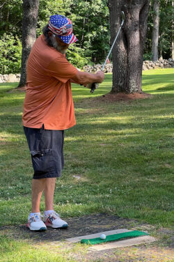 Player in American flag decorated ball cap does a practice swing at tee