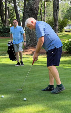 Mike Ramini putts ball into hole while Sean Dumont carries golf bag ready to head to the next hole