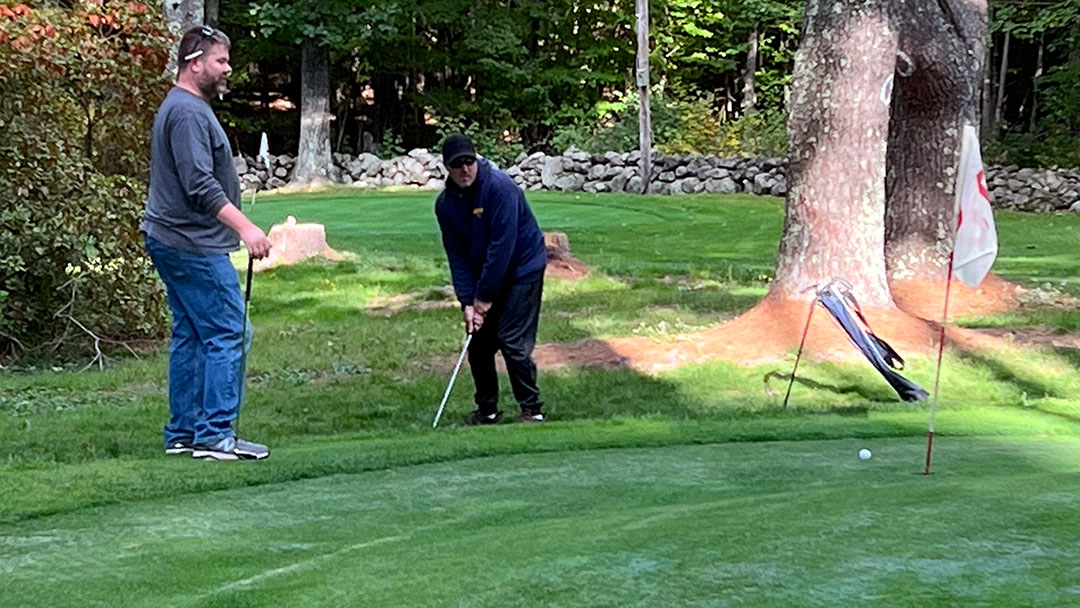 Player chips a shot towards the hole while teammate looks on