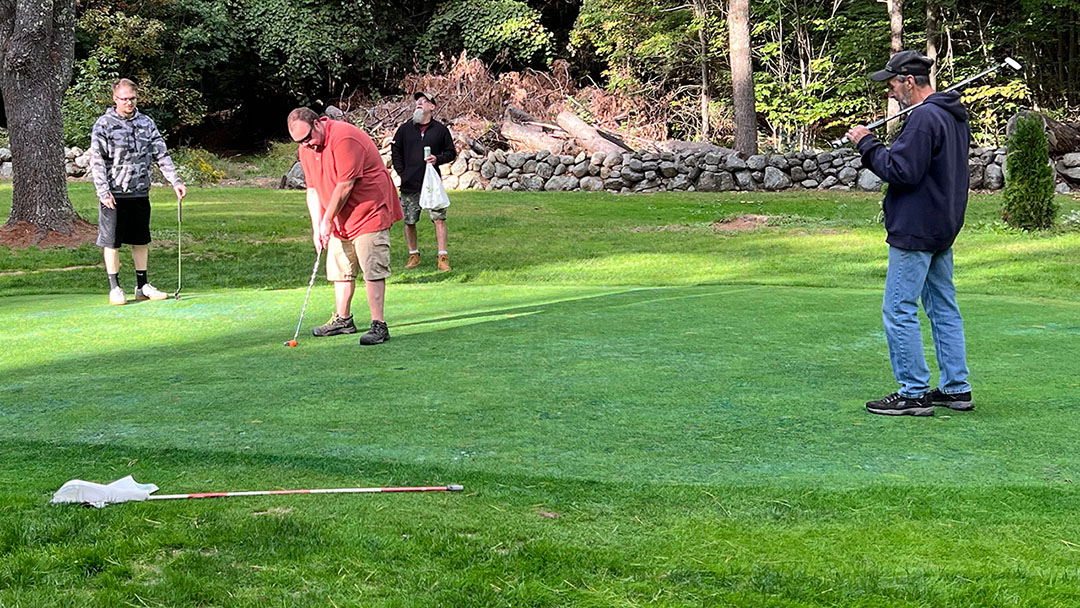 player lines up putt while teammates look on